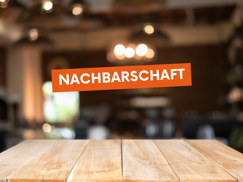 Der Text „Nachbarschaft“ steht in einem orangen Textblock. Im Hintergrund sind ein Holztisch und eine unscharfe Beleuchtung abgebildet.