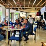 Veranstaltung „Repair fair - Reparieren und Aufmöbeln“ in der wunderwerft. 13 Personen, die an Tischen sitzen oder stehen reparieren unterschiedliche Dinge und unterhalten sich dabei.