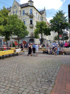 Menschen stehen, sitzen und reden beim Straßenpicknick. Mehrere Bierzeltgarnituren wurden auf der Kreuzung angeordnet und mit Tischdecken ausgestattet.
