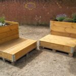 Zwei Pflanzmöbel – Kombiniert aus einem Hochbeet und einer Sitzfläche – befinden sich vor einer Steinwand des Leher Pausenhofs. Die Hochbeete der Pflanzmöbel wurden frisch mit Blumen und Kräutern bepflanzt.