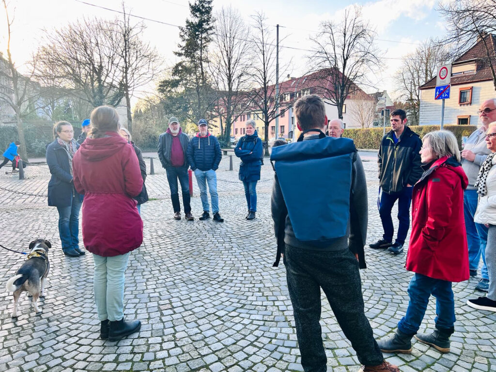 Rundgang mit mehreren Personen durch das Goethequartier. Miriam Gieseking erzählt Fakten zur Geschichte Lehes. Im Hintergrund sieht man Häuser und Bäume.