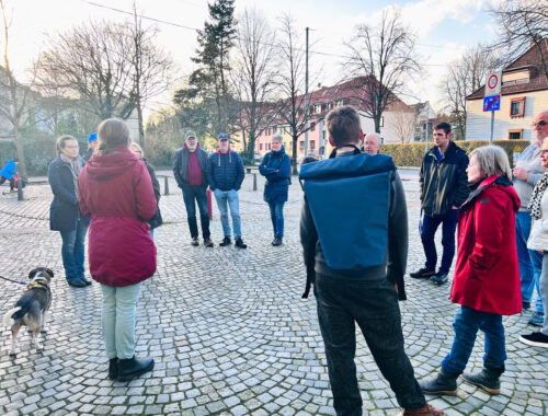 Rundgang mit mehreren Personen durch das Goethequartier. Miriam Gieseking erzählt Fakten zur Geschichte Lehes. Im Hintergrund sieht man Häuser und Bäume.