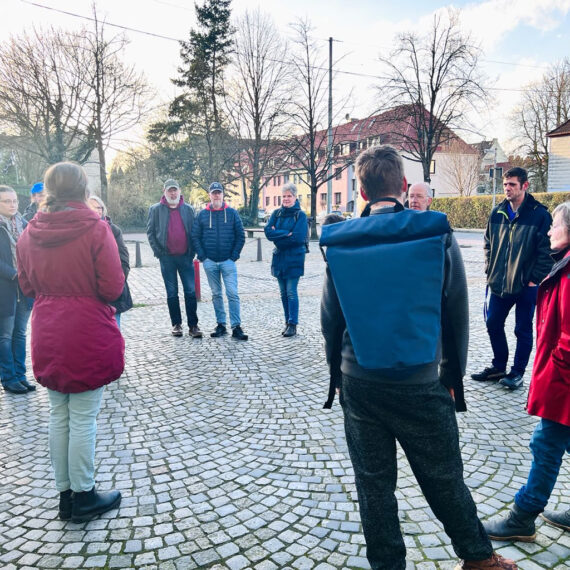 Rundgang mit mehreren Personen durch das Goethequartier. Miriam Gieseking erzählt Fakten zur Geschichte Lehes. Im Hintergrund sieht man Häuser und Bäume.