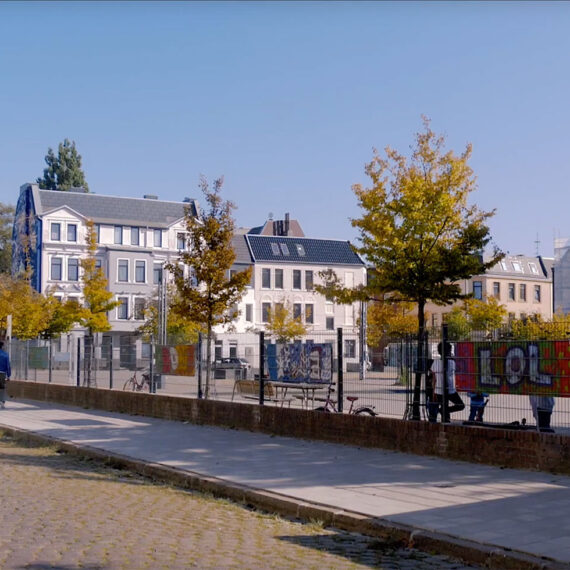Blick auf den Leher Pausenhof. Hinter einem Zaun sind Spielgerüste, -geräte, Fahrräder und Kinder zu sehen.