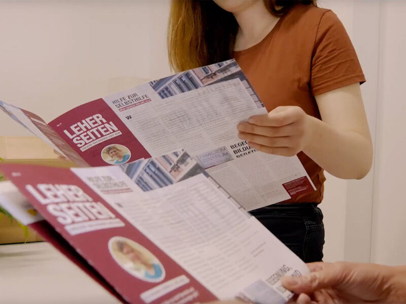 Zwei Personen schauen sich jeweils eine Ausgabe der Leher Seiten an.