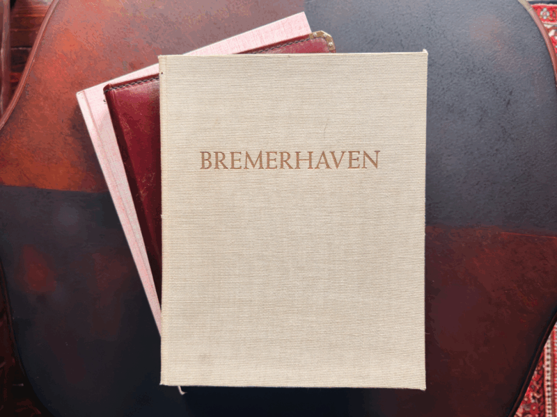 Alte Bücher liegen auf einem Tisch, auf dem obersten steht der Titel 