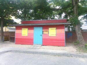 Die sogenannte „Bunte Bude“ vor einer Steinmauer des Leher Pausenhofs – eingerahmt von Bäumen. Die Bunte Bude verkauft Speisen und Getränke.