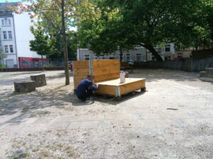 Pflanzmöbel auf dem Leher Pausenhof. Im Vordergrund hockt ein Junge vor der Sitzgelegenheit aus Holz.