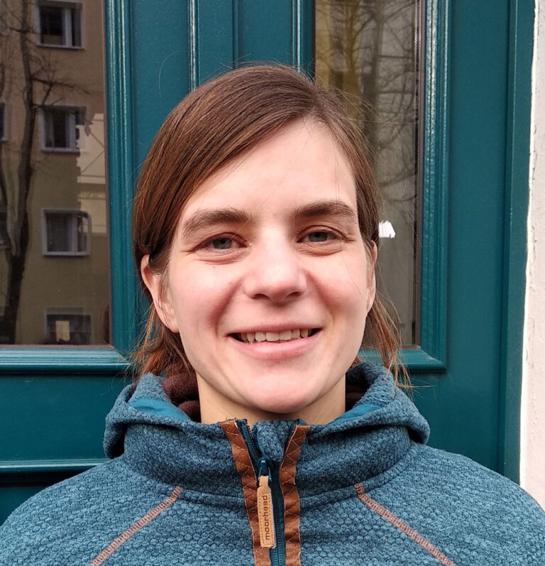 Miriam Gieseking, Quartiersmeisterin in Bremerhaven Lehe, lächelt in die Kamera. Sie steht vor einem blauen Türrahmen und trägt eine blaue Jacke.
