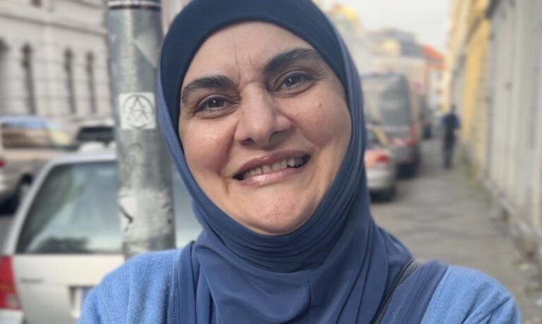 Eine Frau mit einem blauen Kopftuch lächelt offen in die Kamera. Sie steht in einer Straße des Goetheviertels.