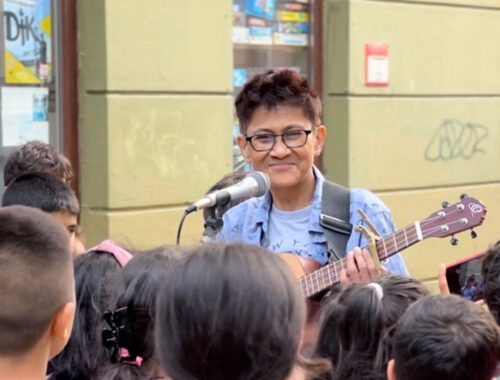 Eine Person spielt Gitarre und singt und vor ihr stehen viele Kinder