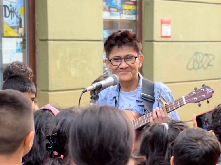 Eine Person spielt Gitarre und singt und vor ihr stehen viele Kinder