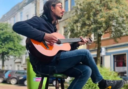 Eine Person sitzt auf einem Barhocker und spielt Gitarre