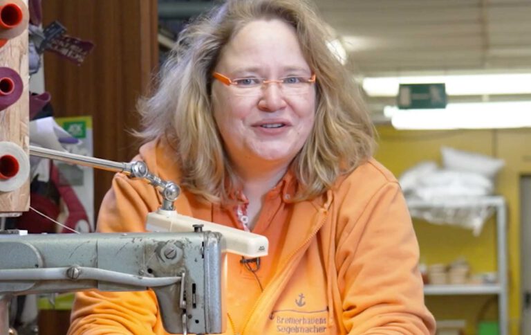Eva Erkenberg lächelt in die Kamera. Sie sitzt hinter einer alten Nähmaschine.