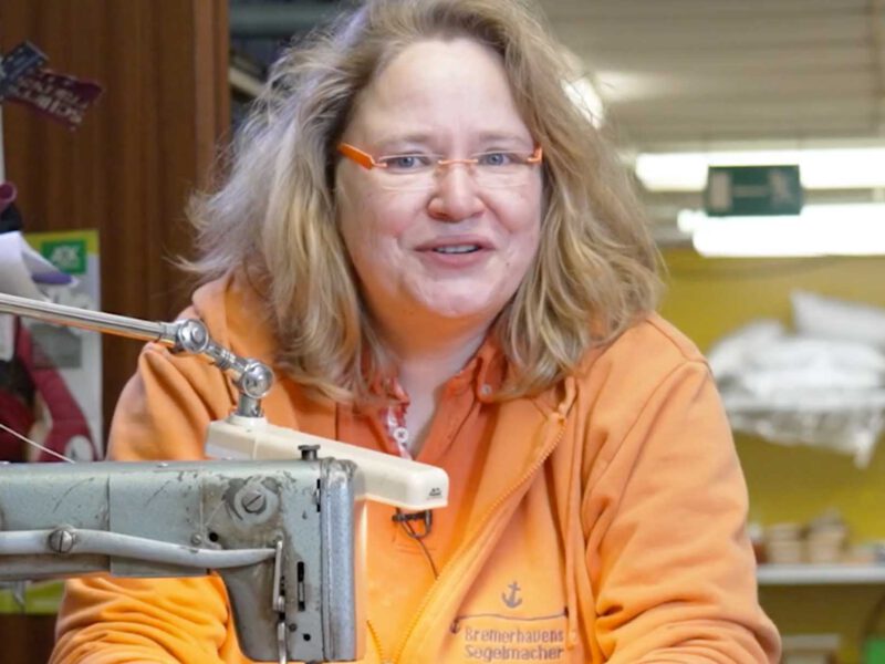 Eva Erkenberg lächelt in die Kamera. Sie sitzt hinter einer alten Nähmaschine.
