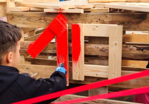 Ein Kind malt ein selbstgebautes Holzhaus rot an