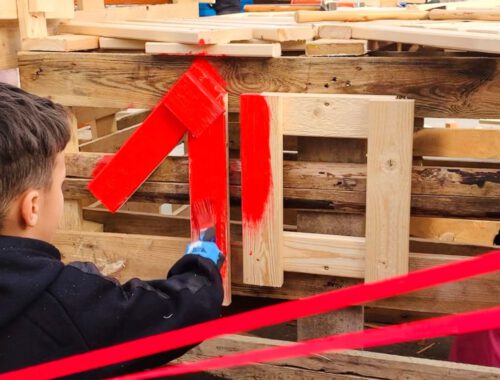 Ein Kind malt ein selbstgebautes Holzhaus rot an