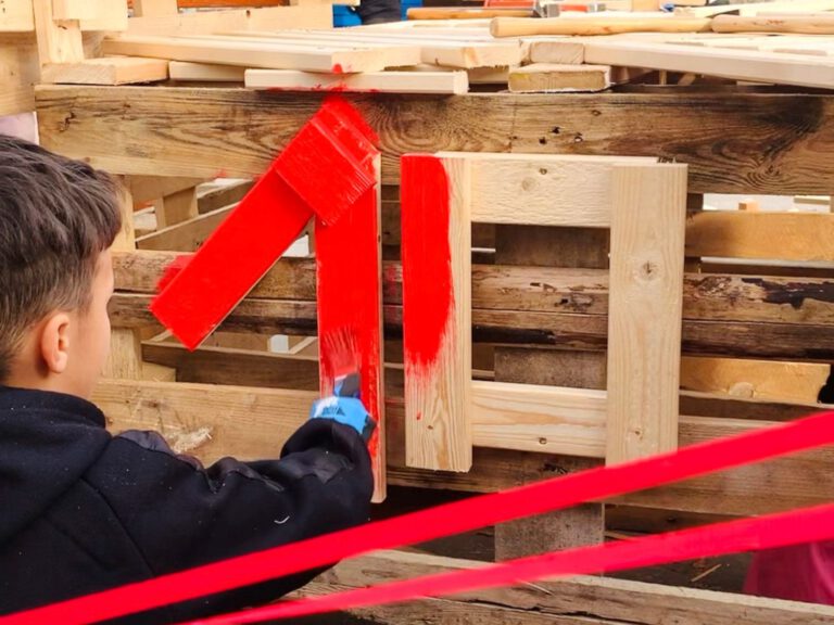 Ein Kind malt ein selbstgebautes Holzhaus rot an