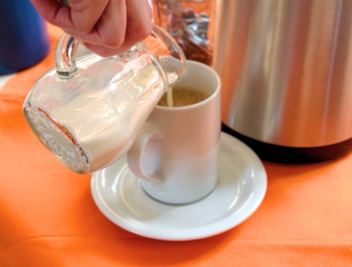 Jemand schenkt Milch in eine Kaffetasse ein