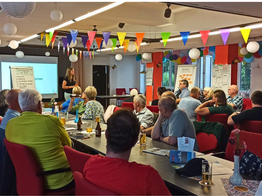Viele Menschen sitzen an Tischen als Gäste bei der Stadtteilkonferenz