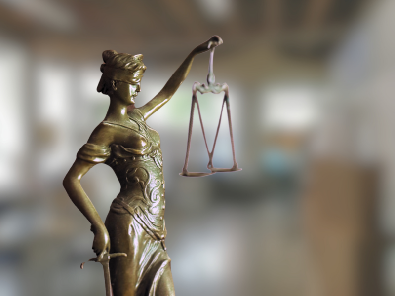 Eine Justitia vor einem verschwommenen Bürohintergrund