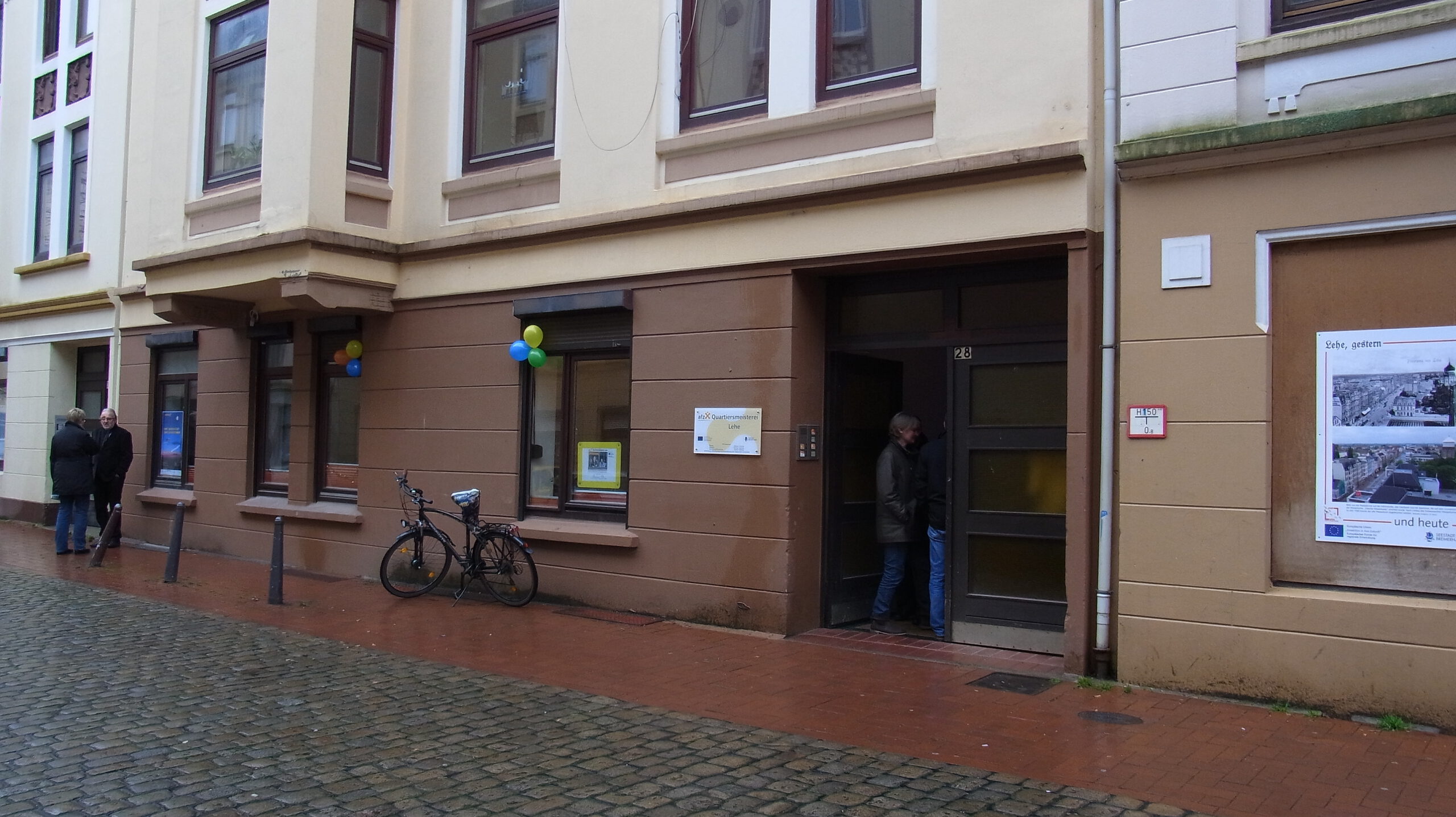 Erdgeschoss Außenansicht der Uhlandstraße 28. Die Altbaufassade ist braun und beige, im Eingang stehen ein paar Menschen.