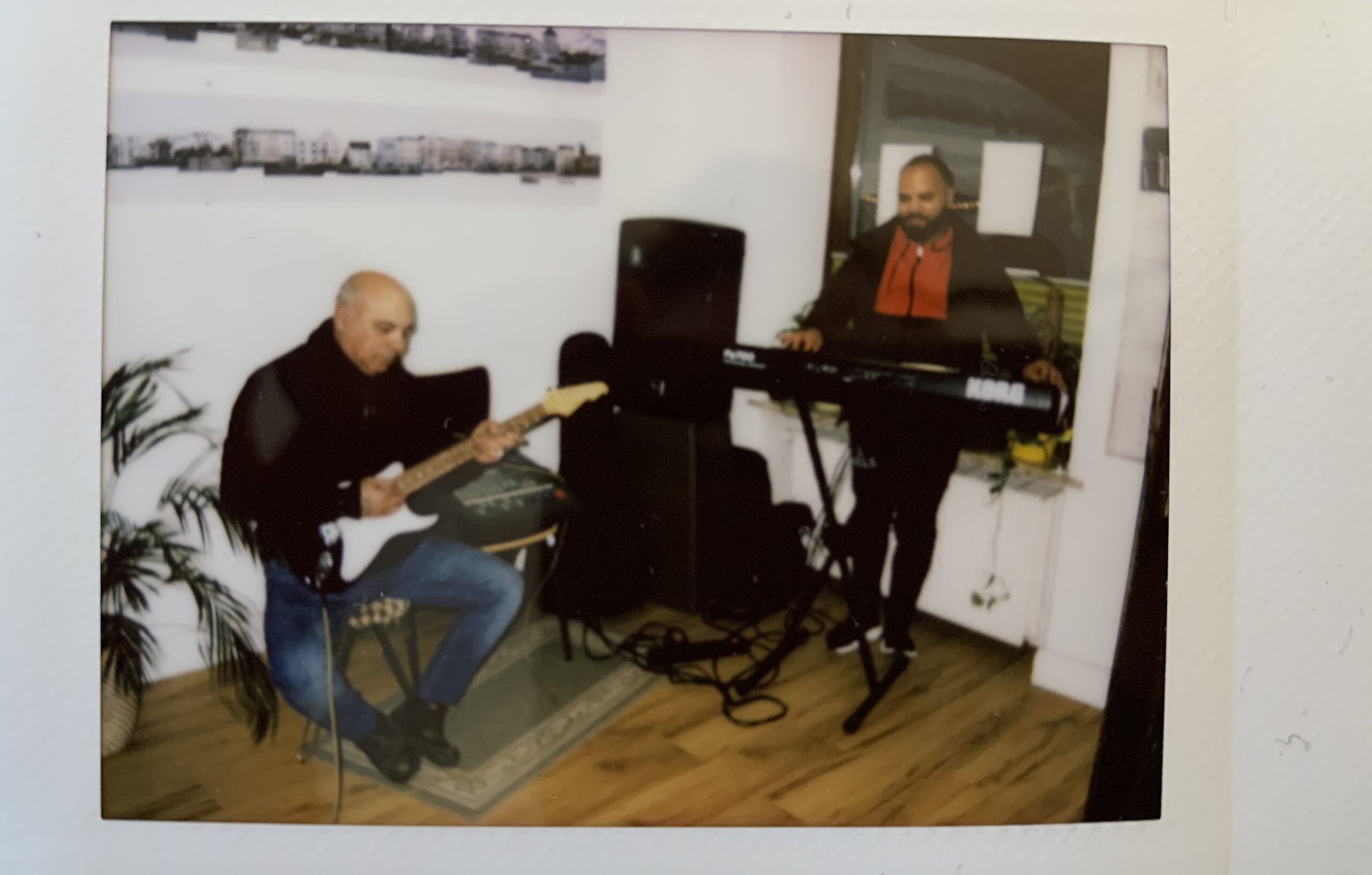 In einem Eingangsbereich sitzt ein Mann auf einem Stuhl und spielt Gitarre und ein anderer Mann steht hinter einem Keyboard.