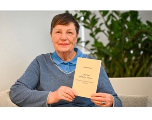 Porträtfoto einer älteren Frau mit kurzen braunen Haaren, die ihr Buch 