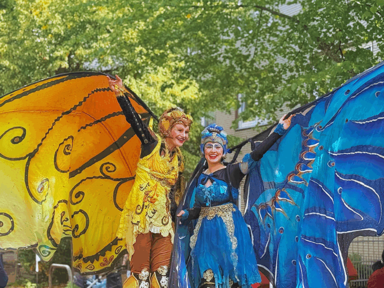 Zwei Personen verkleidet als große Schmetterlinge stehen auf der Straße und lachen