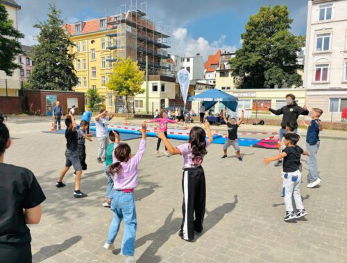 Kinder stehen in einem Kreis und machen gemeinsam Aufwärmübungen für den Urban Sports Day
