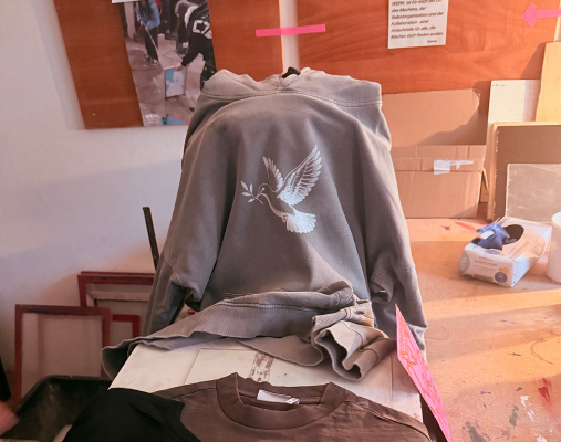 Kleidungsstücke liegen in einer Werkstatt, auf ihnen sind weiße Friedenstauben gedruckt