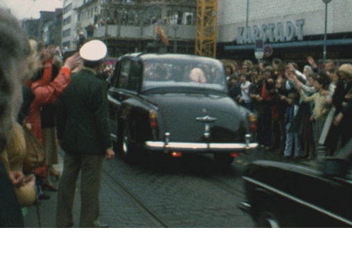 Straße vor einem Kaufhaus mit Menschenmassen und einem Auto wo die Queen drin sitzt