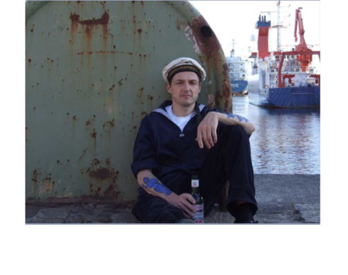 Matrose sitzend vor Schiffsbug mit Schiffen im Hintergrund