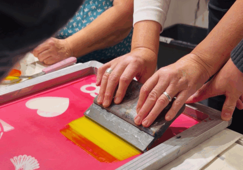 Mehrere Hände an einem Tisch sind dabei einen Spatel über einen Sieb zu ziehen