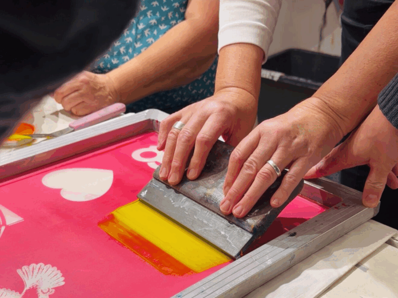 Mehrere Hände an einem Tisch sind dabei einen Spatel über einen Sieb zu ziehen