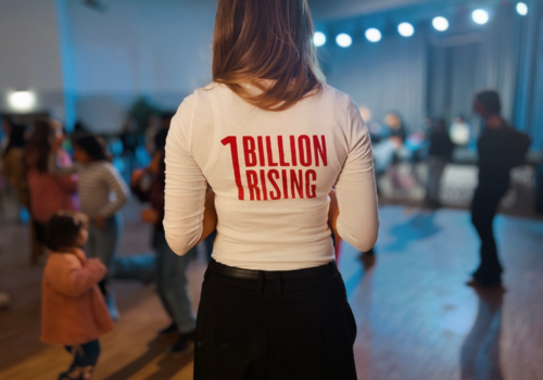 Es ist der Rücken einer Person zu sehen die ein weißes Oberteil trägt auf dem in rot 