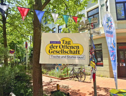Ein Banner vom Tag der offenen Gesellschaft hängt zwischen einem Baum und einem Straßenschild. es ist Sommer auf der Goethestraße