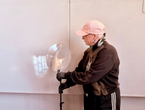 Eine Person hält ein Stativ mit einer Lichtreflektierenden Linse vor eine weißen Wand auf die ein umgedrehtes Kirchenfenster projiziert wird