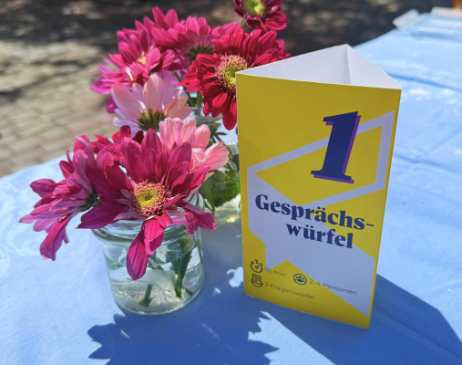 Ein Tisch auf dem Blumen und ein Infoaufsteller zu Gesprächswürfeln steht