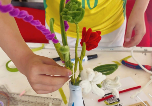 Hände arrangieren Blumen aus Pfeiffenreinigern in einer bemalten Vase