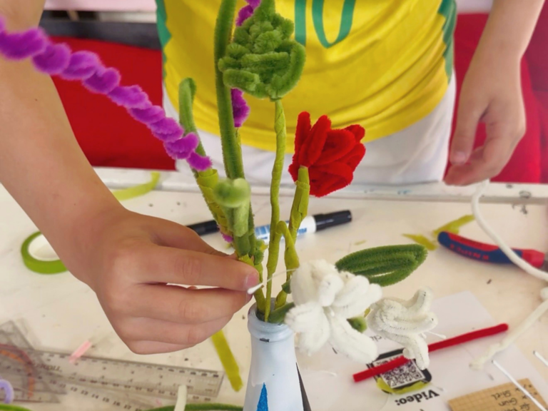Hände arrangieren Blumen aus Pfeiffenreinigern in einer bemalten Vase