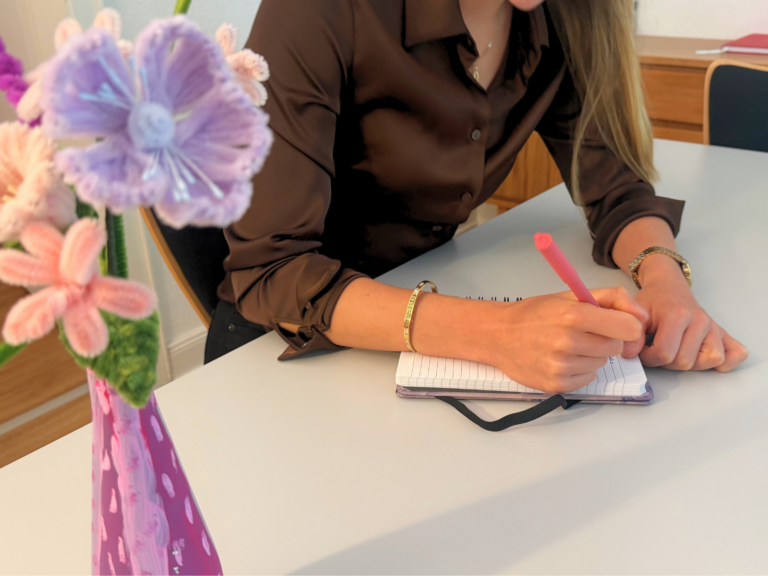 Eine Person sitzt an einem Tisch und schreibt in ein Notizbuch