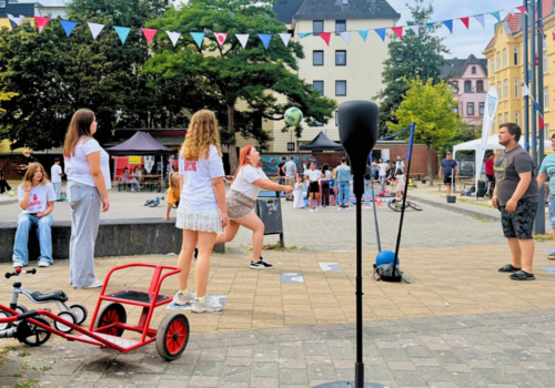 Viele Kinder und Jugendliche stehen auf einem Platz und probieren verschiedene Sportarten aus