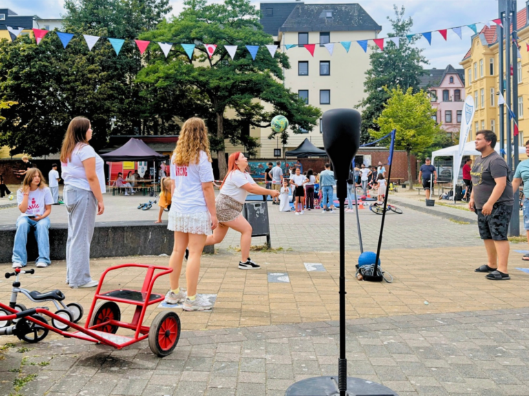 Viele Kinder und Jugendliche stehen auf einem Platz und probieren verschiedene Sportarten aus