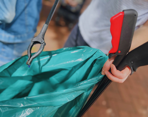 Eina Hand hält eine Mülltüte und einen Müllgreifer