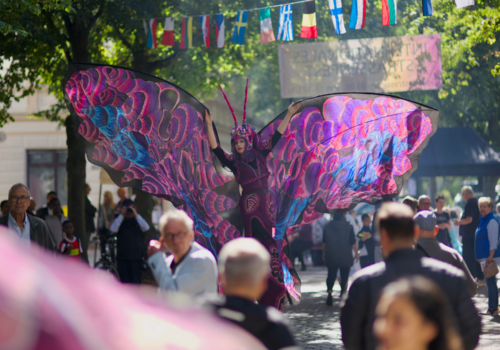 Viele Menschen auf der Goethestraße und in der mitte eine als Schmetterling verkleidete Stelzenläuferin
