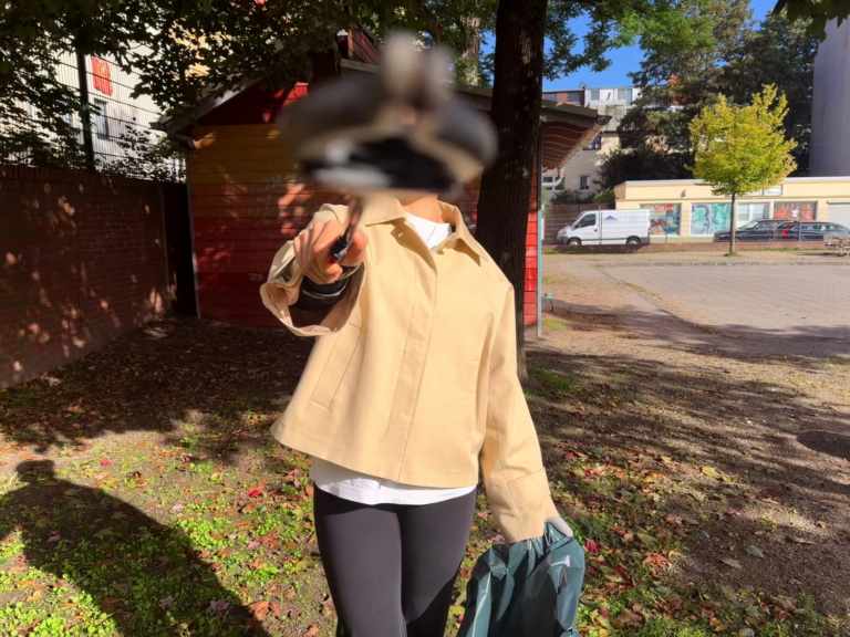 Eine Person hält eine Mülltüte in der Hand und einen Greifer vor ihr Gesicht